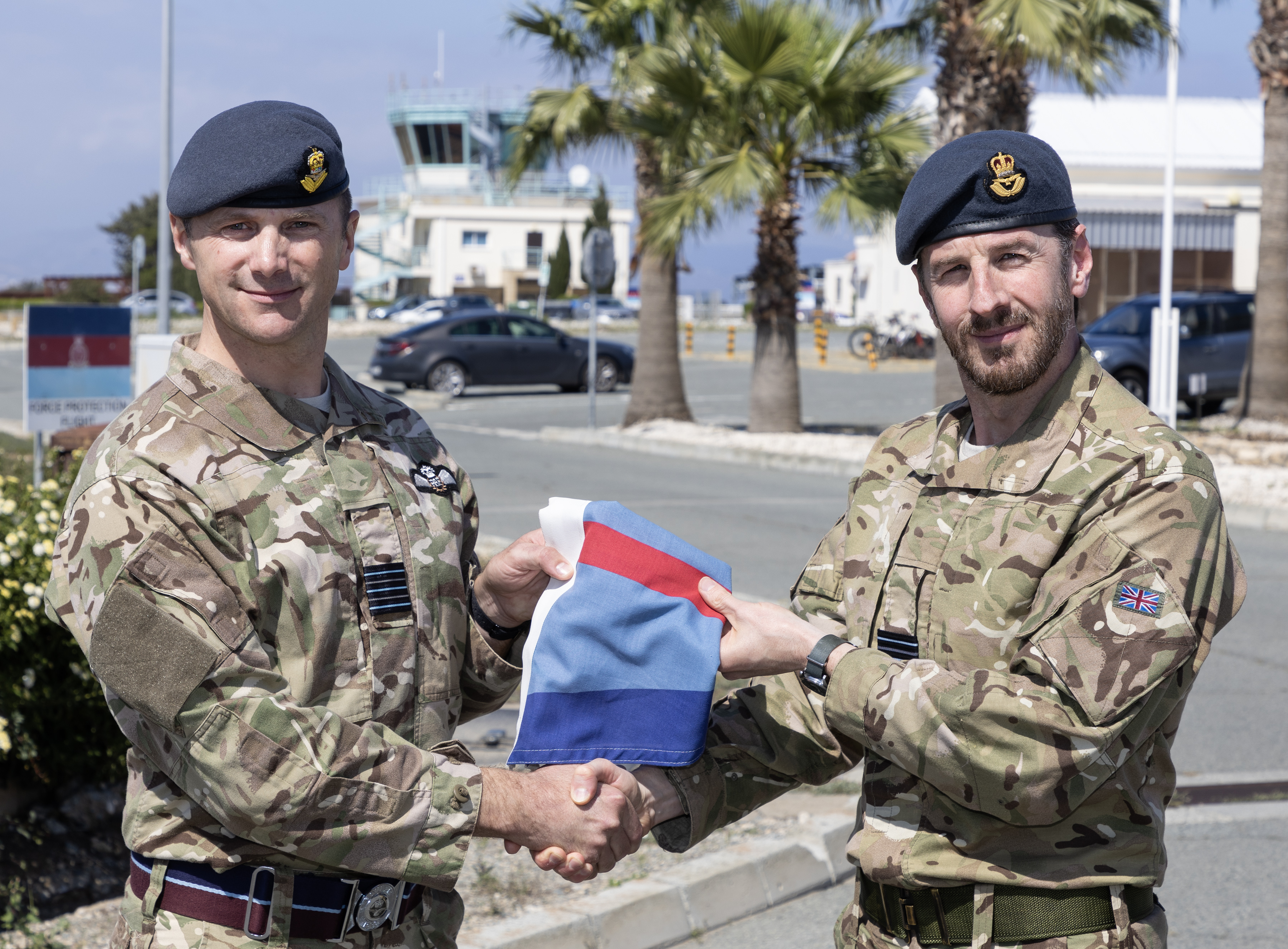 Image shows RAF personnel shaking hands while holding a flag. 